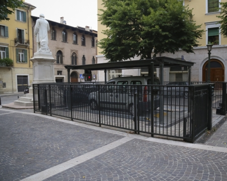 Baia d'ingresso a livello strada con balaustra di protezione per un sistema di parcheggio automatico sotterraneo in una piazza pubblica a Verona.